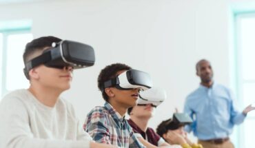 View of a classroom with children using virtual reality headsets along with a trainer standing besides them