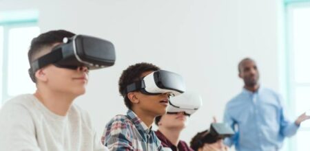 View of a classroom with children using virtual reality headsets along with a trainer standing besides them